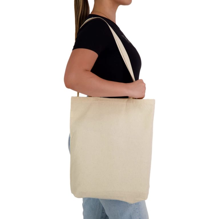 A woman holds a natural-coloured tote bag with long handles. The bag features a logo.